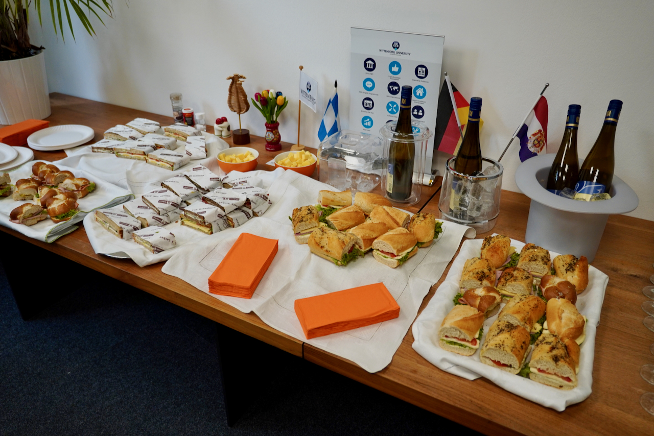 DHV00872 Buffet table with assorted finger sandwiches, wraps, cheese cubes, and orange napkins at a corporate event setup.