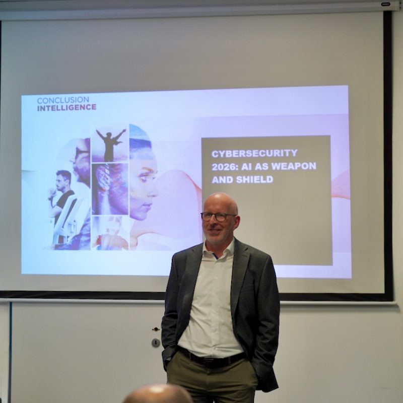 Male presenter in a blazer speaks in front of a projected slide on cybersecurity.