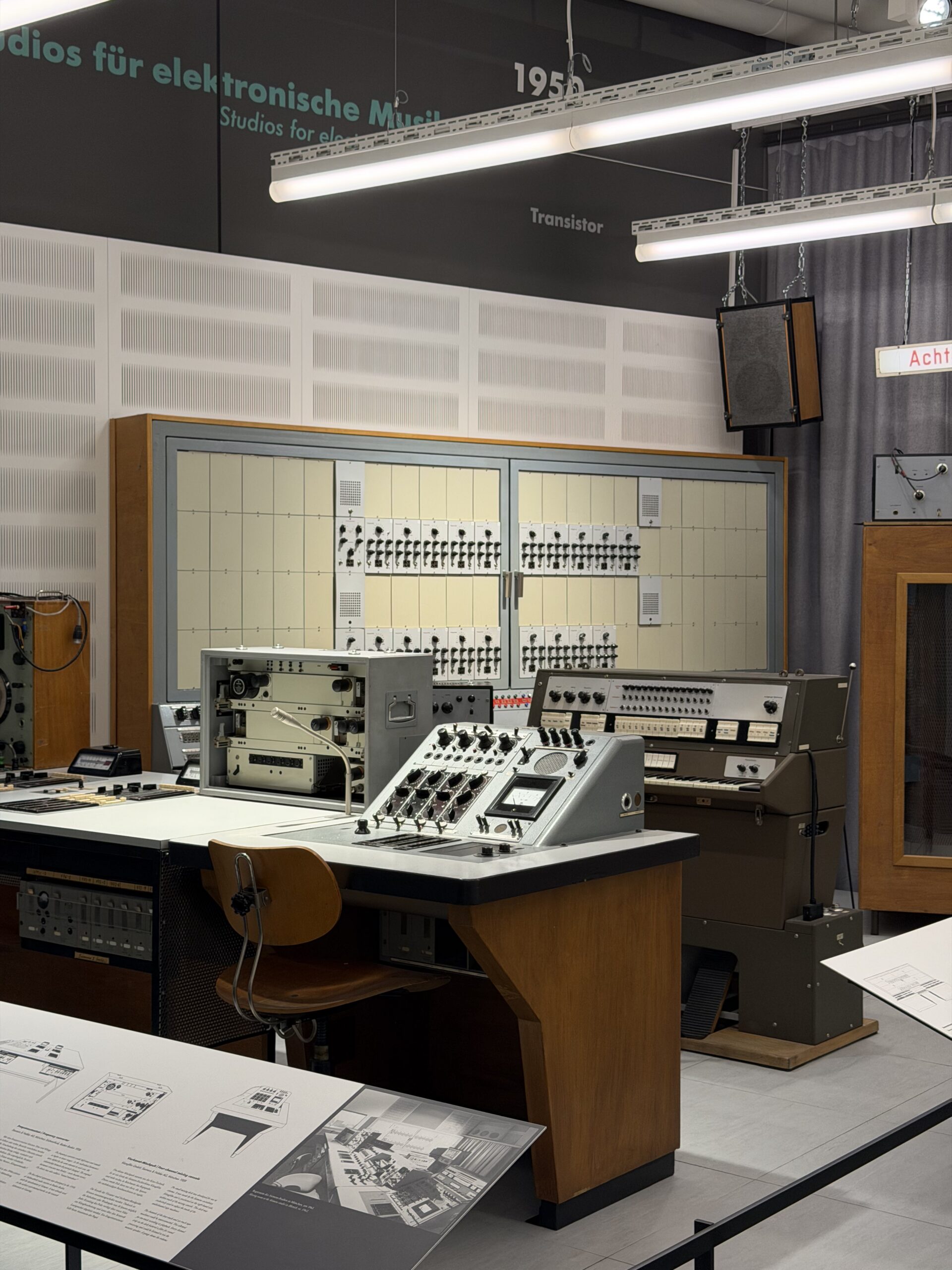 Vintage modular synthesizer rig on a workbench with multiple panels, knobs, and patch cables in a museum-style exhibit