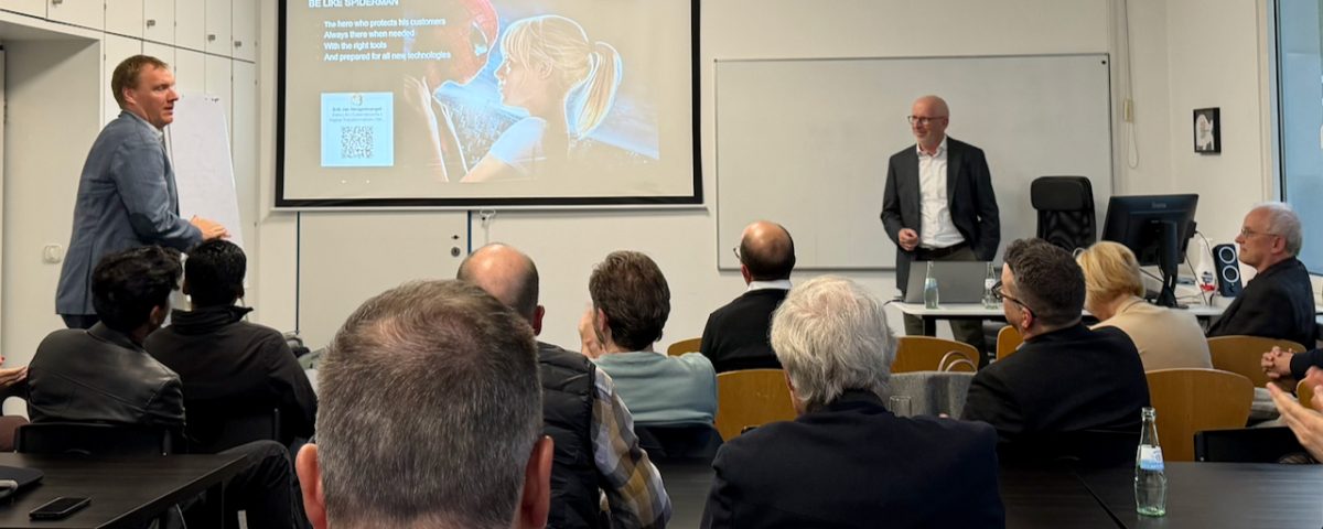 Conference room presentation with two men at the front and a projected slide about Spider-Man's tactics/text appears on screen.