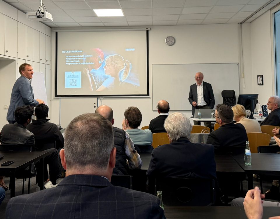Conference room presentation with two men at the front and a projected slide about Spider-Man's tactics/text appears on screen.