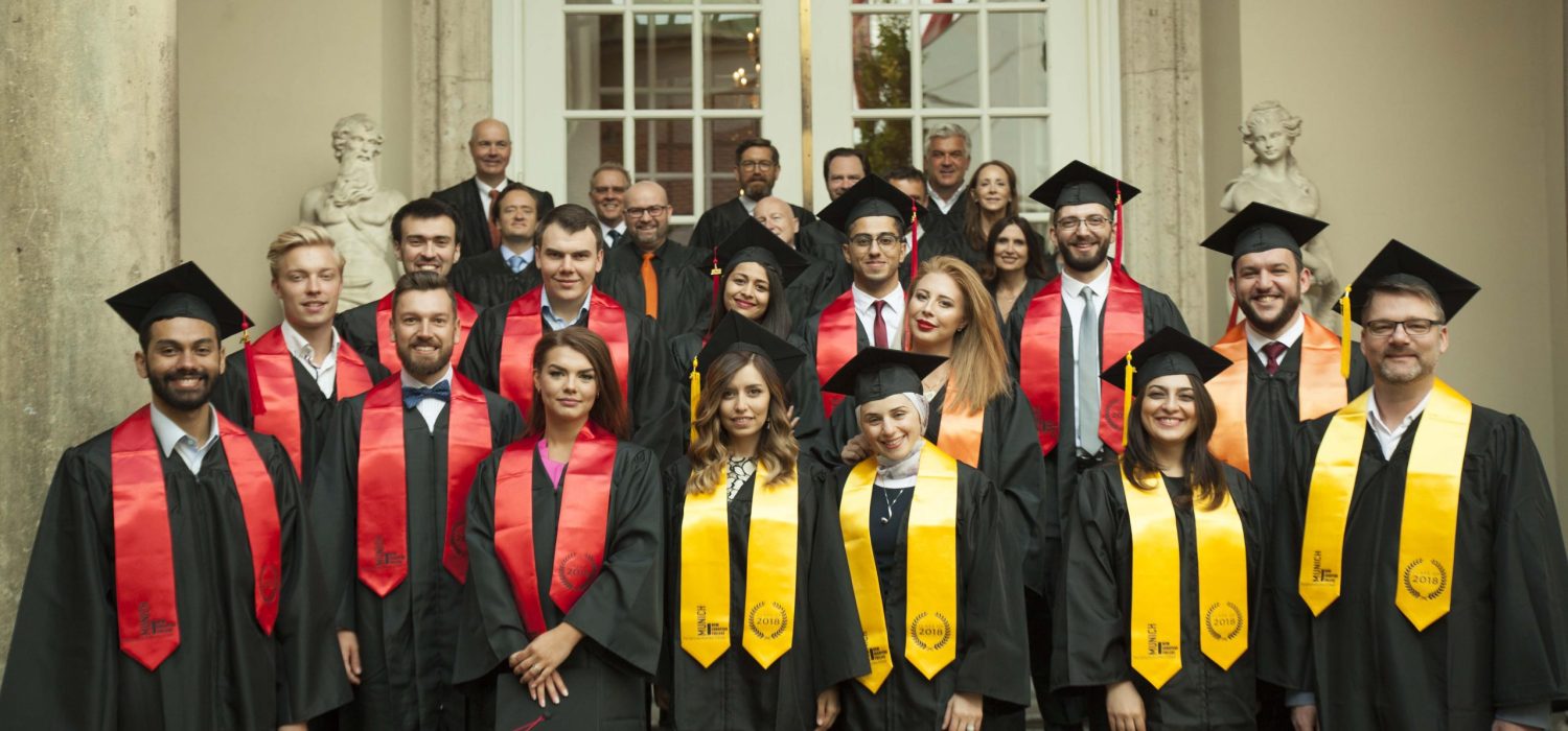 Group photo of graduates in black gowns with red and yellow sashes and mortarboards posing on building steps outside a stately entrance.